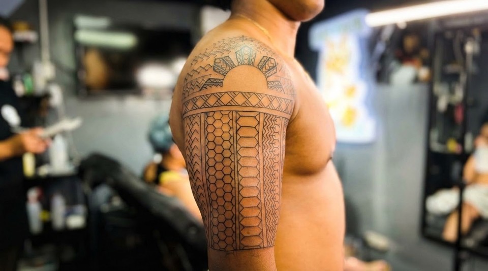 A person's arm with a traditional Filipino sun tattoo on the shoulder and intricate geometric patterns on the sleeve.