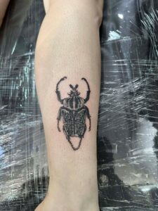 A realistic black and grey illustrative tattoo of a beetle on a person's forearm.