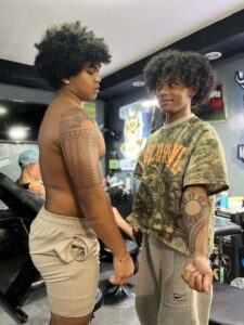 Two young men with traditional tattoos standing in a tattoo parlor.