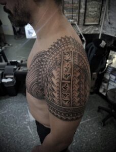 A man's shoulder and chest featuring a detailed black ink tribal tattoo with traditional patterns.