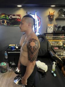 A man with a large tribal tattoo on his left arm stands in a tattoo shop in Boracay, showcasing tattoo designs for men.