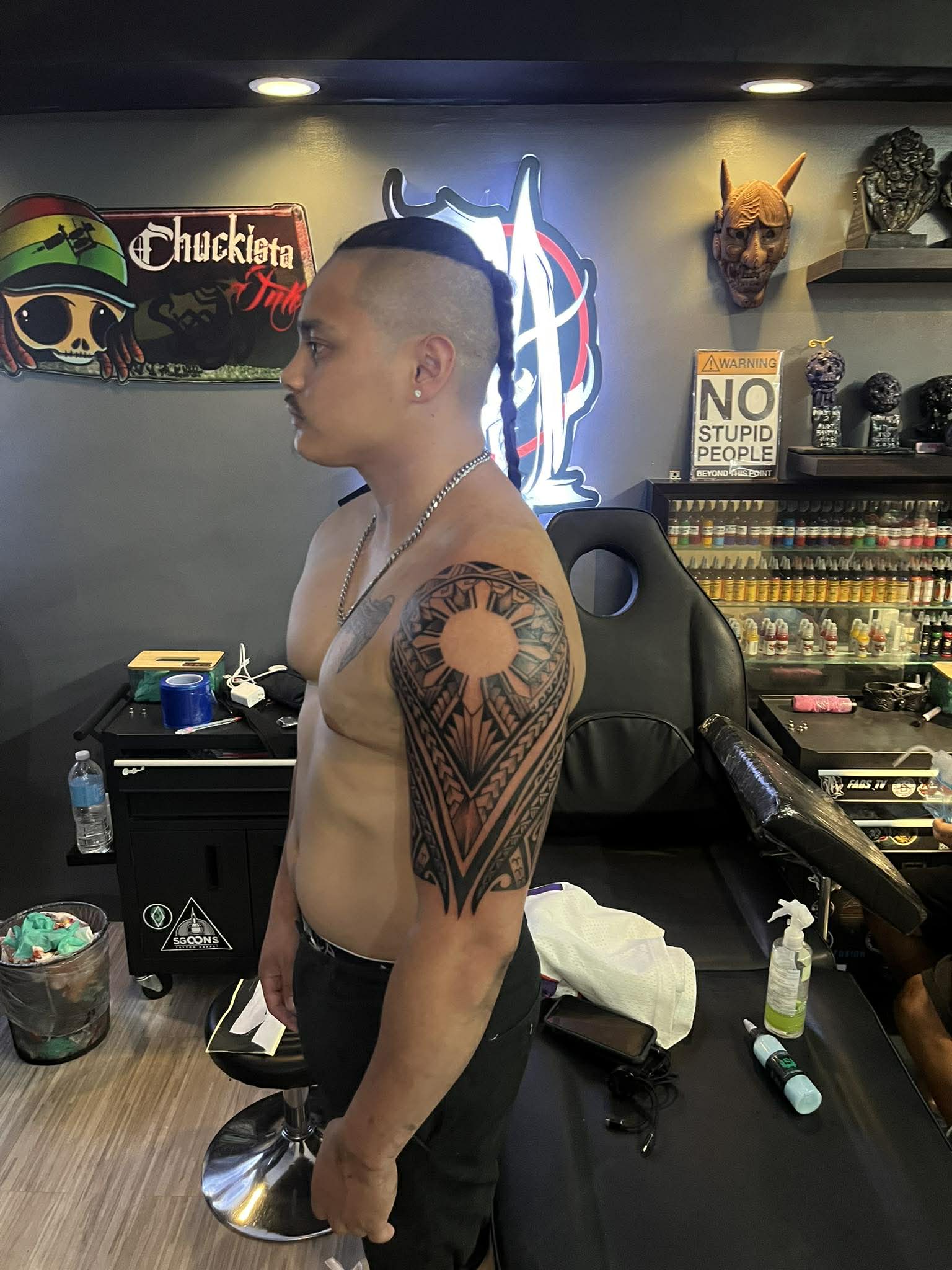 A man with a large tribal tattoo on his left arm stands in a tattoo shop in Boracay, showcasing tattoo designs for men.