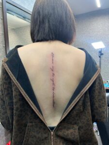Minimalist script tattoo on the back, featuring precise micro-lettering in a clean cursive font by Kurt Bayeta.
