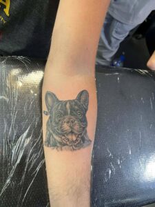 A realistic black and grey pet portrait tattoo of a French Bulldog on a forearm, custom-designed and tattooed by Kurt Bayeta at Octosquidink Boracay.