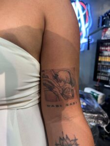 A person's arm with a black and white tattoo of a scene from "Spirited Away" with the text "WABI SABI" below it.