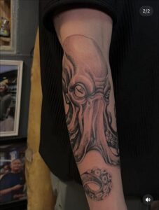 A highly detailed black and gray tattoo of an octopus covers the arm of an outstretched limb.