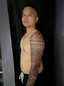A close-up of a man's arm, highlighting the intricate patterns of a tribal tattoo sleeve.