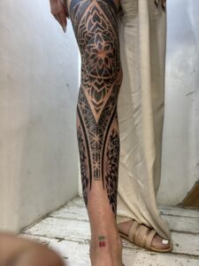 Front view of a full-leg geometric sleeve tattoo, featuring symmetrical mandala patterns on the knee and shin with bold blackwork borders.