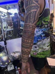 A person with a full tribal tattoo on their left arm, standing in a tattoo parlor.
