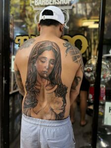 A person with a large tattoo of the Virgin Mary with roses on their back, in front of Octosquidink Tattoo Boracay.