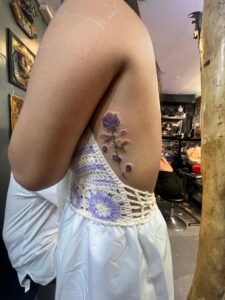 Purple rose realism rib tattoo with falling petals in vibrant color.