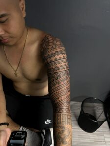 A close-up of a man's arm, highlighting the intricate patterns of a tribal tattoo sleeve.