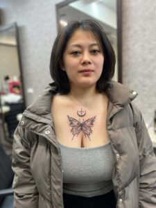 A woman with a butterfly and crescent moon tattoo on her chest, wearing a puffer jacket.