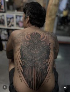 A large full-back tattoo of a winged warrior in ornate plate armor, holding a broadsword downward, featuring detailed shading and large feathered wings.