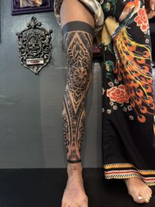 Front view of a full-leg sleeve tattoo featuring intricate blackwork geometric patterns and mandalas centered on the knee and extending down the shin.