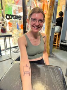 A smiling client showcasing a fresh fine-line tattoo of an artist's easel on her forearm, custom-designed and tattooed by Kurt Bayeta at Octosquidink Boracay.