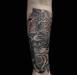 A black and white tattoo of a leopard's head and a rose on a person's arm.