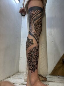 Side profile of a full-leg sleeve tattoo featuring heavy blackwork bands and large, intricate mandala patterns on the thigh, calf, and shin.