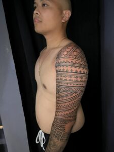 A close-up of a man's arm, highlighting the intricate patterns of a tribal tattoo sleeve.