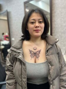 A woman with a butterfly and crescent moon tattoo on her chest, wearing a puffer jacket.